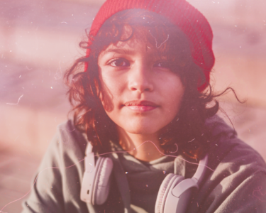 Teenage girl with brown hair and a red beanie, looking pensively to camera